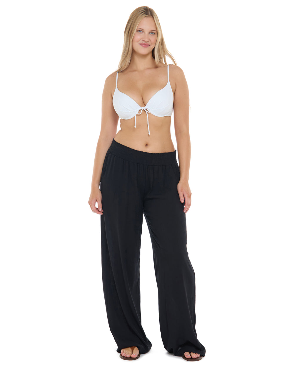 A woman modeling a two-piece swimwear set consisting of a white triangle bikini top with a front tie and black wide-leg swim pants, shot against a solid white background.